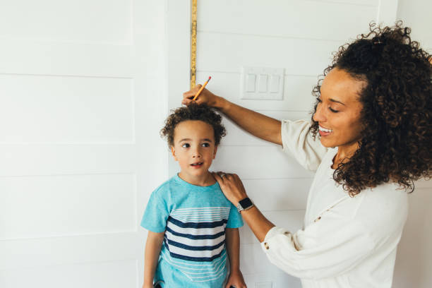 Mother Measuring Height of Son A mom measures her son against a ruler and wall to see how tall he is inside their home. The boy is growing fast at 4 years old and is excited to grow and learn with his mom teaching him. boy height measure stock pictures, royalty-free photos & images