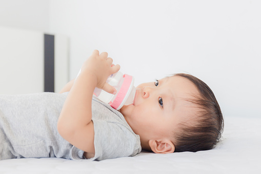 Close up of Adorable baby boy drinking milk from a bottle on the bed