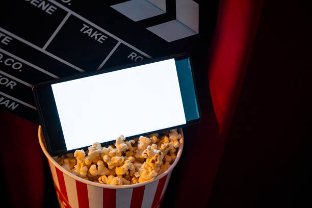 istock mobile phone with empty white bright screen with popcorn bucket and movie clapper board. Concept of streaming TV on internet phone. 1244106812