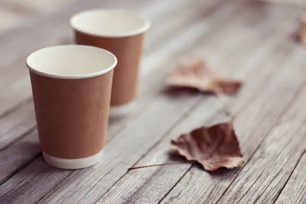 Photo of two paper cups standing on wooden table in outdoors cafe