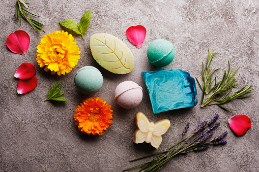 Bath spa accessories on rustic background, colorful bath bombs and soap bars with flowers and herbs.