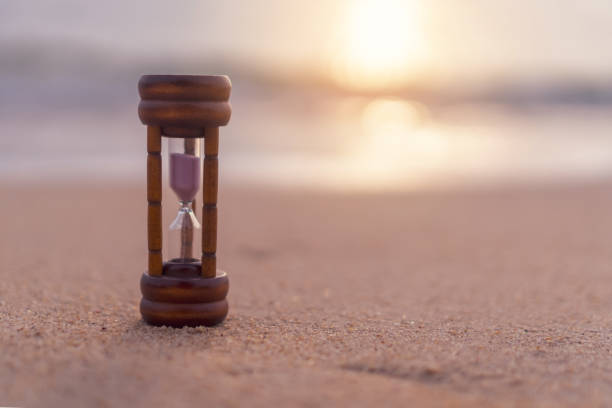 istock Small hourglass show time is flowing on sand beach texture background. 1244222136