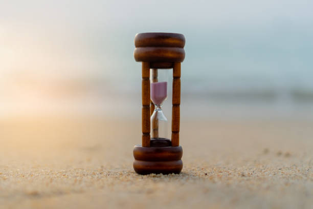 istock Small hourglass show time is flowing on sand beach texture background. 1244222406