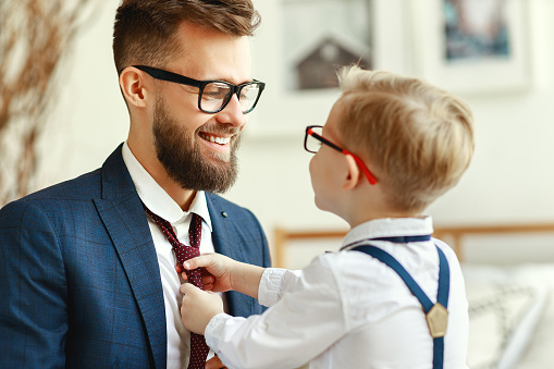 happy family on father's day. happy son helps dad tie a necktie at home
