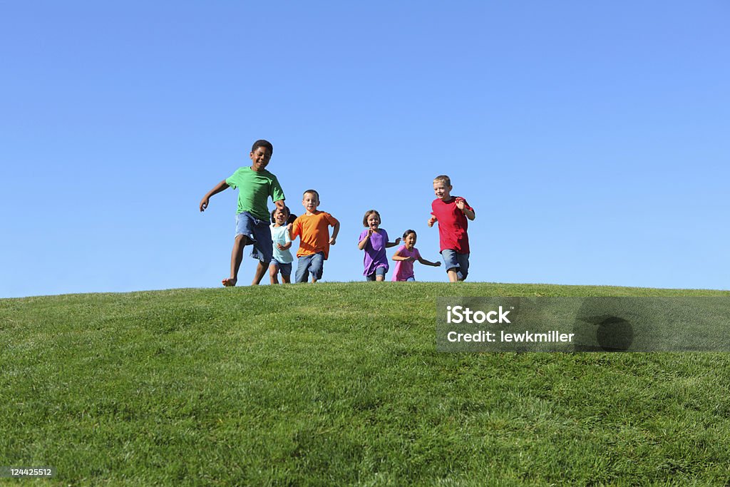 Group of multi-ethnic kids running together Group of multi-ethnic kids running together, on grass hill with blue sky Child Stock Photo