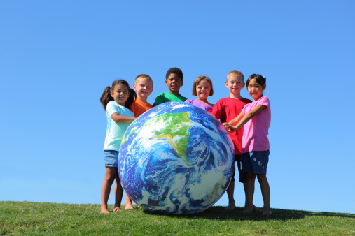 Portrait of multi-ethnic kids with large earth ball, on grass hill with blue sky