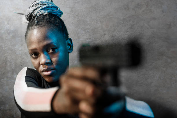 retrato de estilo cinematográfico de hollywood de joven atractiva y segura de sí misma mujer afroamericana negro sosteniendo el arma como agente federal especial o mafioso apuntando la pistola - gun women handgun armed forces fotografías e imágenes de stock