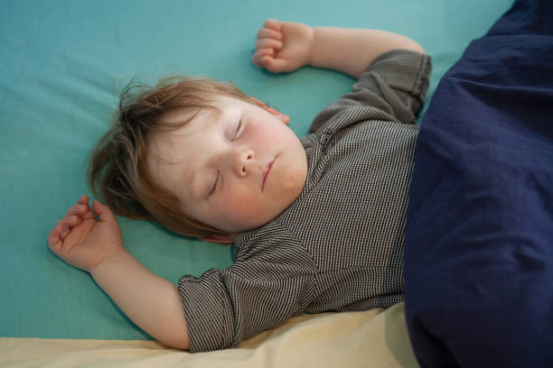 Very tired little boy crashed out asleep on his bed
