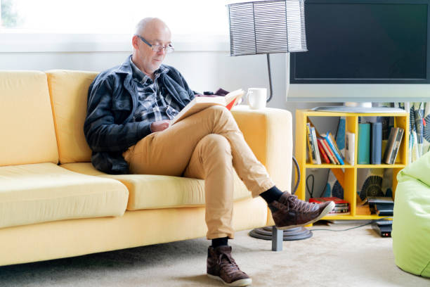 istock Relaxed senior man on yellow sofa reading a book 1244333688