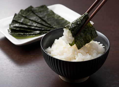 Rice in a teacup set against a wooden backdrop and wrapped with chopsticks in seaweed. Breakfast in Japan