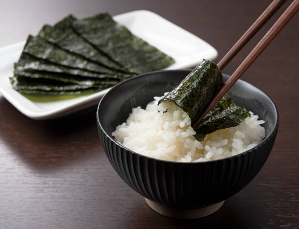 木の背景に置かれた茶碗の中の米は、海藻に箸で包まれています。日本での朝食 - 海藻 ストックフォトと画像