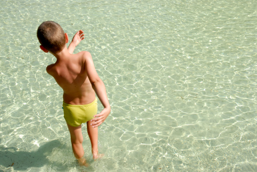 Boy (aged 6 years) walking in a shallow swimming pool.
