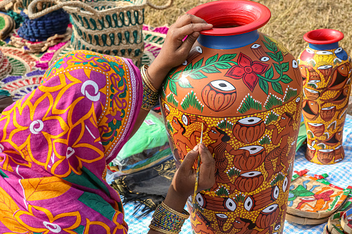 Kolkata, India, November 24, 2019: Rural Indian woman in traditional costume painting a clay pitcher vase for sale at handicraft fair at Kolkata