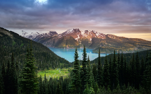Glacial mountain Garibaldi lake with turquoise water in the middle of coniferous forest at sunset.