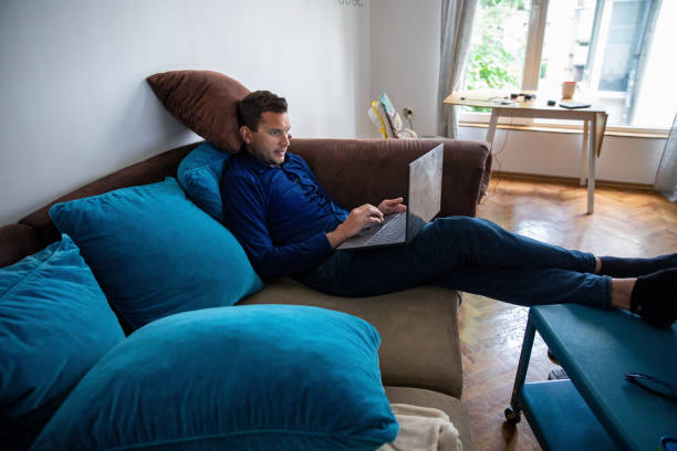 istock Young man lying on sofa while working on laptop from home 1244406715