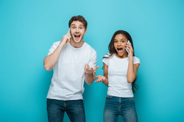 istock excited interracial couple talking on smartphones while standing with open arms on blue background 1244446955