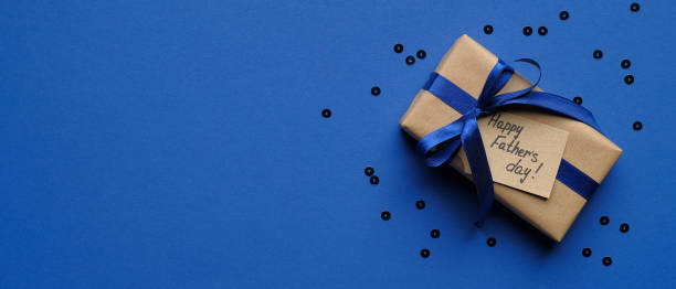 Happy Fathers Day concept. Wide banner mockup with gift box wrapped craft paper with blue ribbon and label Happy Father's Day on blue background with confetti. Fathers Day sale promotion poster design concepto feliz del día del padre. maqueta de pancarta ancha con caja de regalo envuelto papel artesanal con cinta azul y etiqueta happy father's day sobre fondo azul con confeti. diseño de cartel de promoción de la venta del día del padre