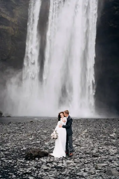 Photo of The groom hugs the bride from behind. Wedding couple near Skogafoss waterfall. Destination Iceland wedding.