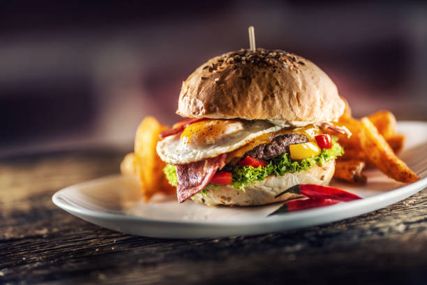 istock Beef burger with fried egg, bacon, cheese, lettuce and peppers in a sesame bun with potato wedges with smoked paprika and extra fresh chilli on the side. 1244493930