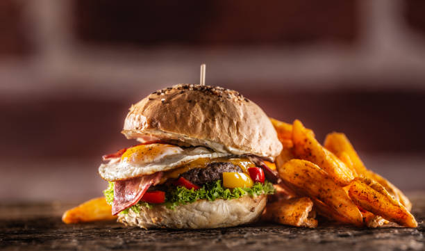 istock Beef burger with fried egg, bacon, cheese, lettuce and peppers in a sesame bun with potato wedges with smoked paprika. 1244494473