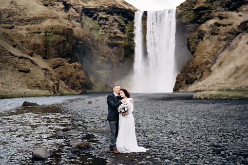 Wedding couple near Skogafoss waterfall. The bride and groom cuddle by the river.