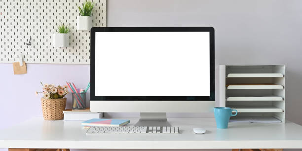 istock Computer monitor with white blank screen putting on white working desk that surrounded by coffee cup, bookshelf, wireless mouse, keyboard, notebook, pencil holder, flowers in wicker basket and books. 1244502201