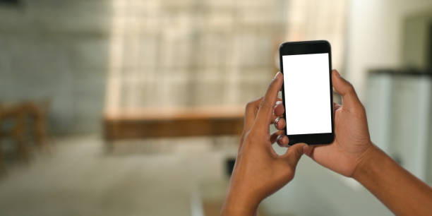 istock Cropped image hands holding cropped black smartphone with white blank screen over blurred comfortable sitting room as background. 1244502237