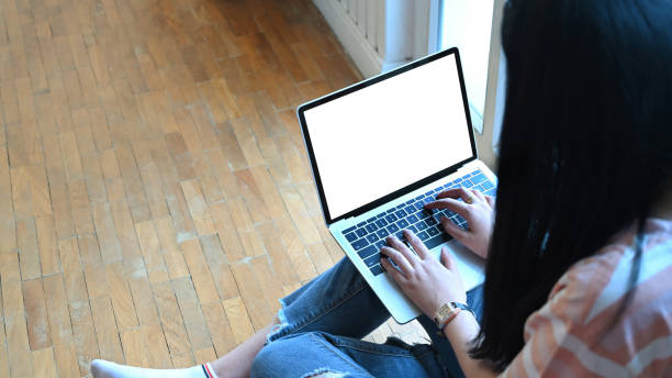 istock Cropped image of creative woman hands using a computer with white bank screen that putting on her lap over comfortable sitting room as background. 1244502262