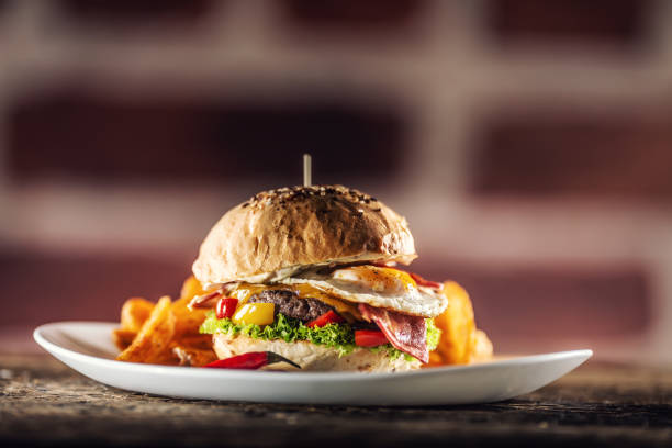 istock Beef burger with fried egg, bacon, cheese, lettuce and peppers in a sesame bun with potato wedges with smoked paprika and extra fresh chilli on the side 1244504439