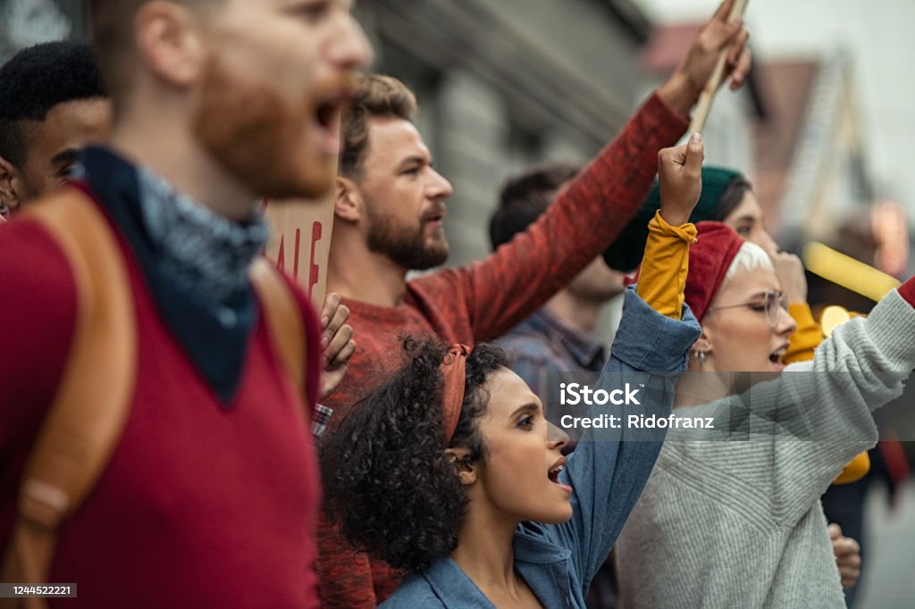 Group of people in rally protesting Side view of group of multiethnic people protesting outdoors with placards and signs. People shouting with banners protest as part of a climate change march. Protestors holding worker rights banners at protest. Protest Stock Photo