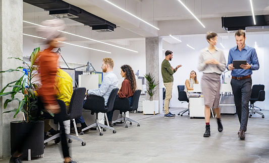 Group of businesswomen and businessmen working in modern office. Interior of busy coworking open space with staff walking and working together. Group of creative men and casual women working in creative agency.