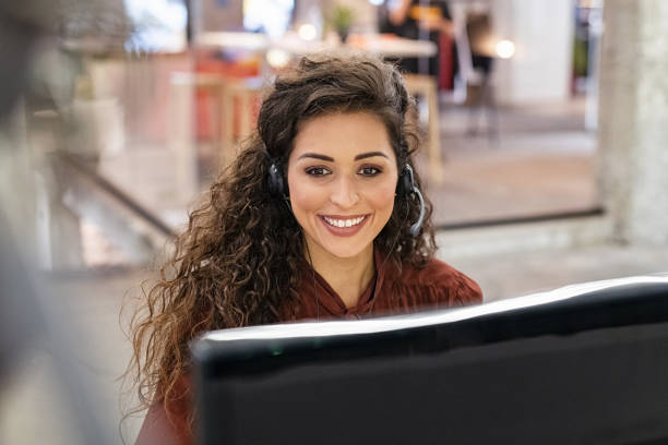 Happy latin woman working with headset Woman customer support operator with headset working on computer. Portrait of cheerful young sales agent in conversation with customer over headset sitting in modern office. Beautiful call center agent working on support online. secretary stock pictures, royalty-free photos & images