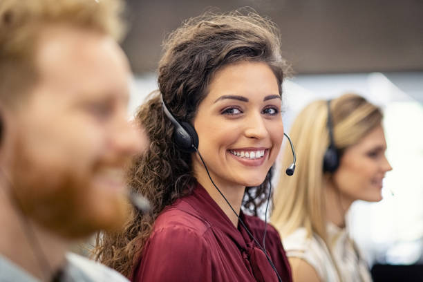 Portrait of smiling woman working in call center Portrait of confident woman working in a call center while looking at camera. Customer care rappresentative working with team in modern office sitting in a row. Support online with latin call center agent. call center stock pictures, royalty-free photos & images