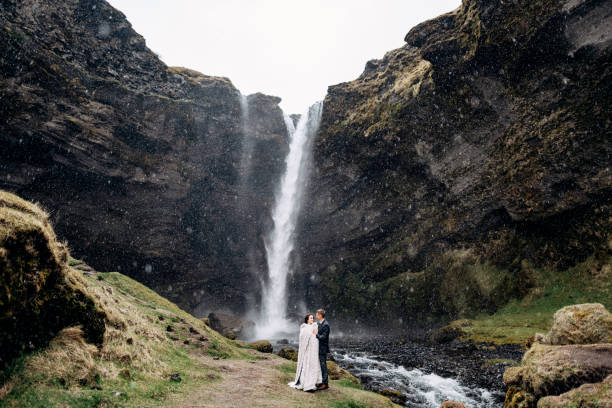 Destination Iceland wedding, near Kvernufoss waterfall. Wedding couple is standing near the waterfall. The groom hugs the bride. A wedding couple stands near a waterfall. The groom hugs the bride. eloping stock pictures, royalty-free photos & images