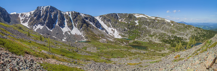 Large panorama of the mountain landscape. Valley with lakes, spring greens and snow on the rocky slopes.