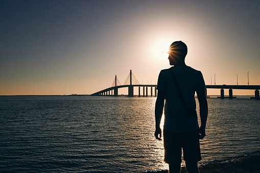 Silhouette of young man on beach against long bridge across sea at sunset. Abu Dhabi, United Arab Emirates