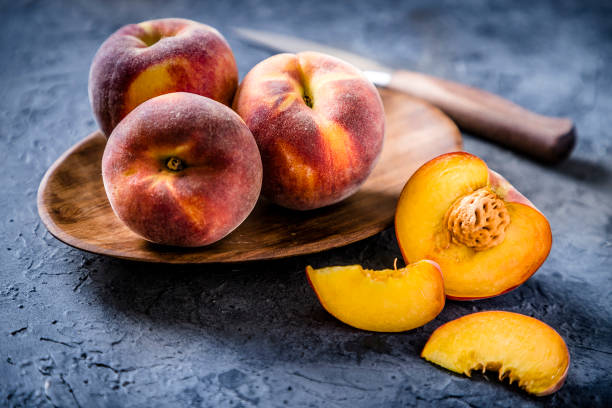 istock Whole and sliced peaches with a kitchen knife on a gray bluish backdrop 1244626100