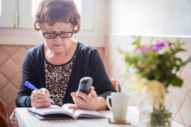 ältere dame hält ein telefon und notizen - personal organizer address book diary glasses stock-fotos und bilder
