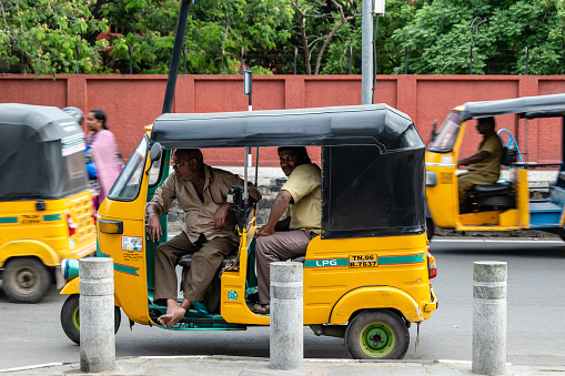 Chennai, Tamil Nadu, India - August 2018: Two auto rickshaw drivers idling inside a vehicle parked by the roadside.