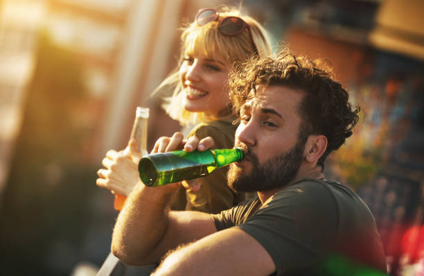 Rooftop party on a summer afternoon. Closeup of a young couple having some beers on a rooftop terrace on a hot summer afternoon ad looking down the street. beer bottle photos stock pictures, royalty-free photos & images