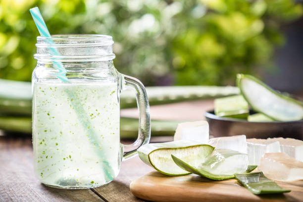 Aloe vera drink Front view of a drinking glass full of an aloe vera drink surrounded by some aloe vera crystals and sliced leaves. A black bowl full of sliced aloe vera leaves is defocused on the background. Predominant color are green and brown. Studio shot taken with Canon EOS 6D Mark II and Canon EF 24-105 mm f/4L aloe vera gel stock pictures, royalty-free photos & images