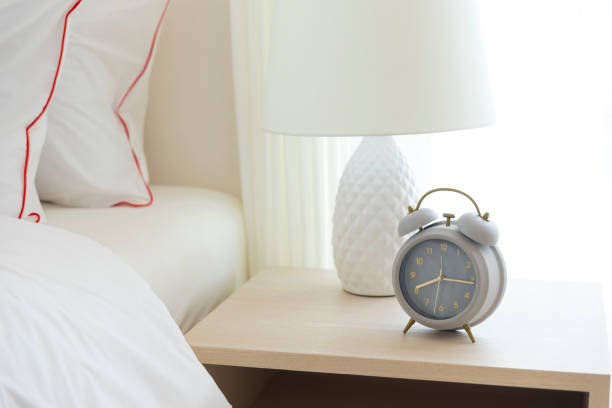 istock Alarm clock on the table beside white cozy bed in bedroom. 1244686552