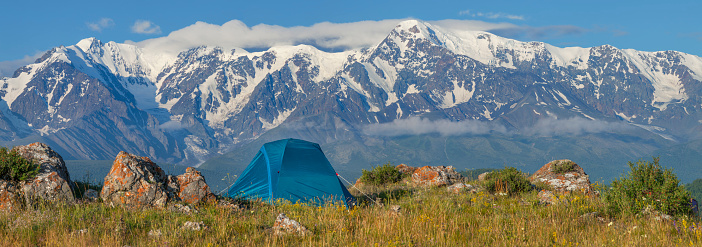 Tent on a background of snow-capped peaks, mountain tourism. Panoramic view.