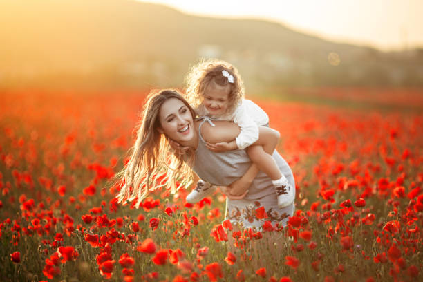 Beautiful child girl with young mother are having fun in field of poppy flowers over sunset lights stock photo