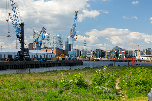 Hamburg, Germany - May 30, 2020: View from the south side of the elbe river to the new hafencity of hamburg. Industrial harbour with warehouses and cranes to the left.