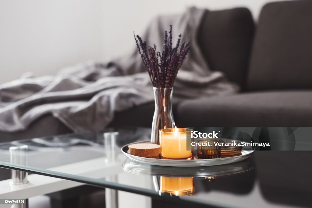 Couchtisch-Design-Idee: Aromakerzen und getrocknetes Lavendelstrauß auf einem Metalltablett, Sofa mit grauer Decke auf dem Hintergrund. Einfache skandinavische Wohnkultur. Hygge-Konzept - Lizenzfrei Kerze Stock-Foto