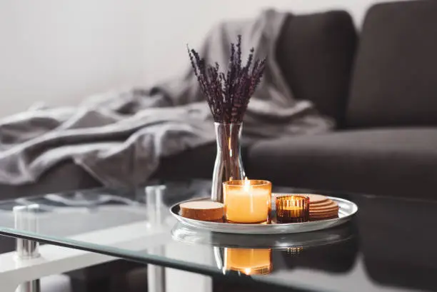 Photo of Coffee table design idea: aroma candles and dried lavender bouquet on a metal tray, sofa with grey blanket on background. Simple Scandinavian home decor. Hygge concept