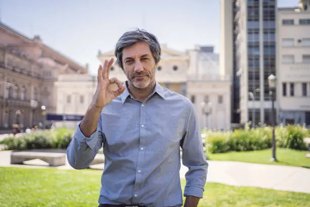 Businessman standing in an outdoor city setting while gesturing an ok sign