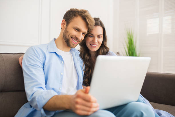 istock Young couple in denim sitting on a sofa watching something online and smiling 1244753935