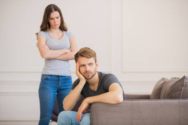 istock Young woman standing with arms clasped while her husband sitting with depressed look 1244754587